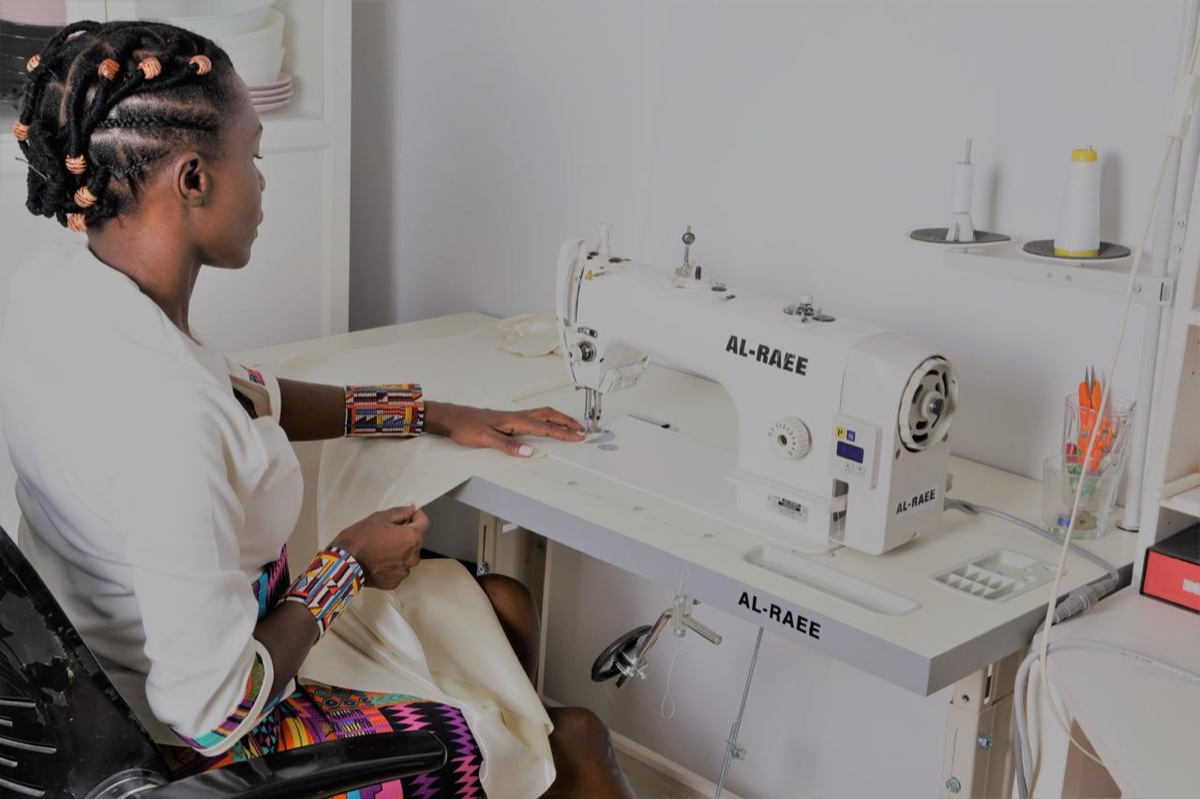 Une couturière guide un tissu clair sous l'aiguille de sa machine, dans son atelier
